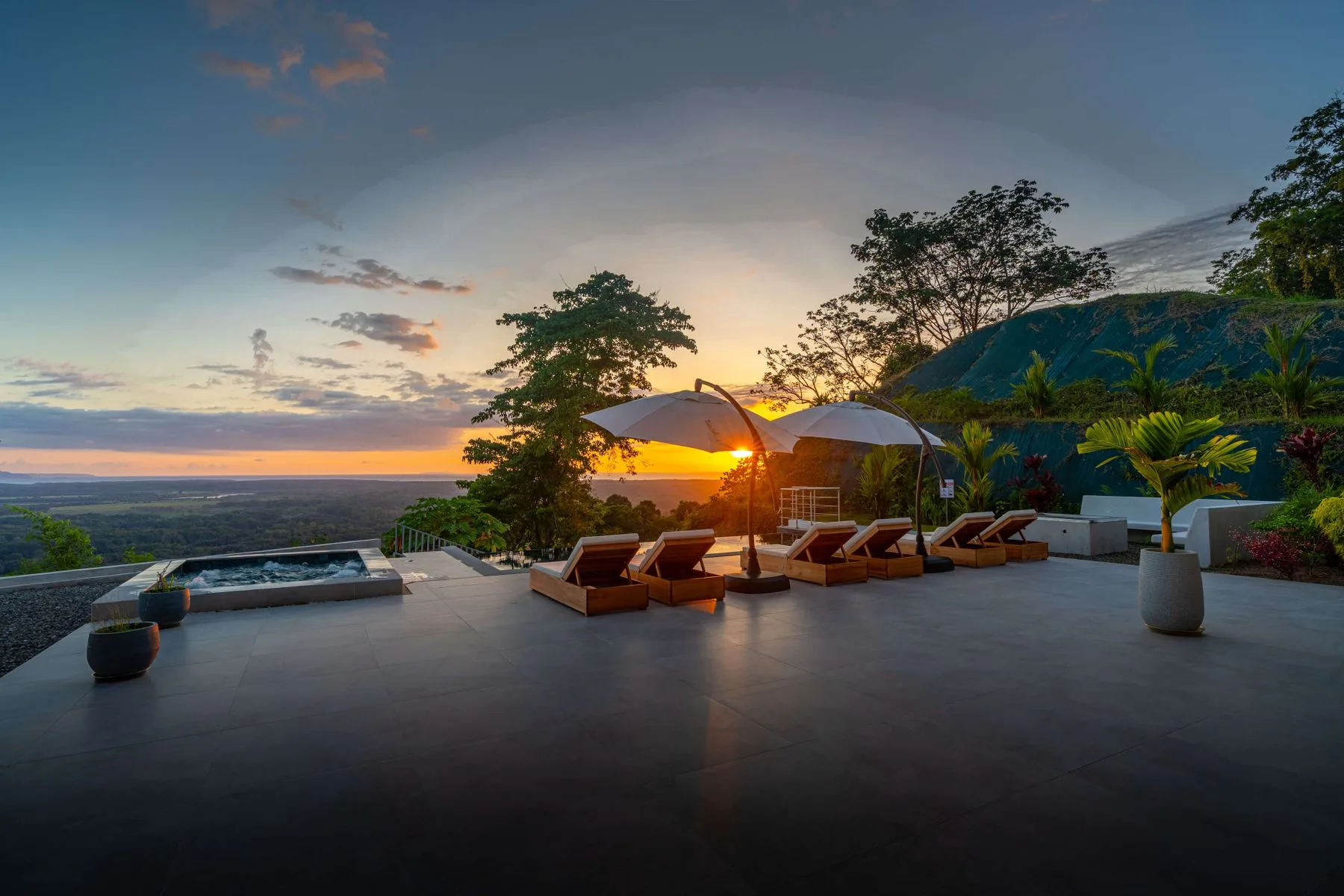 Una terraza al atardecer mira al paisaje, con asientos de descanso y una piscina.