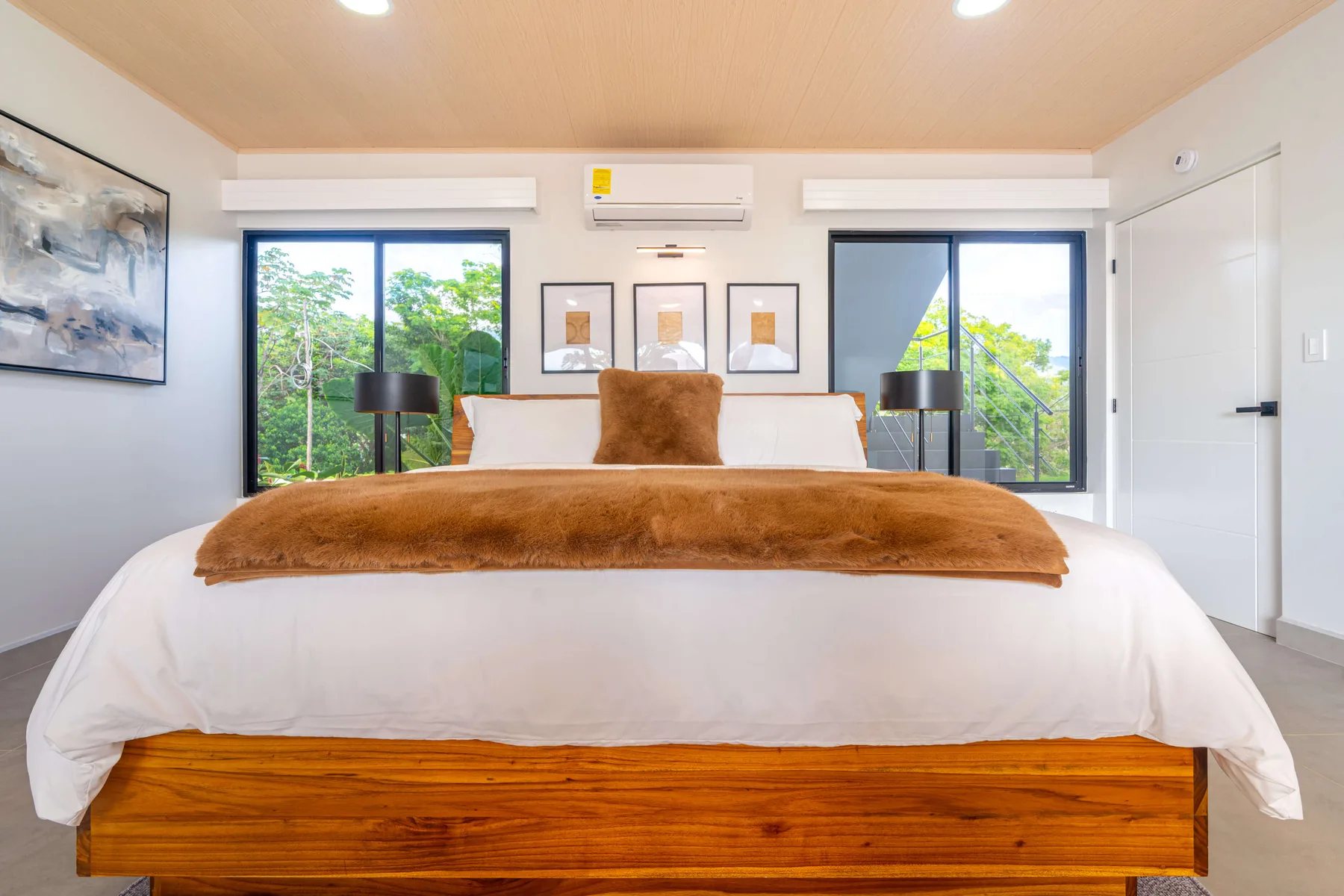 Un dormitorio con una cama grande, cuadros enmarcados y ventanas con vistas a la vegetación.