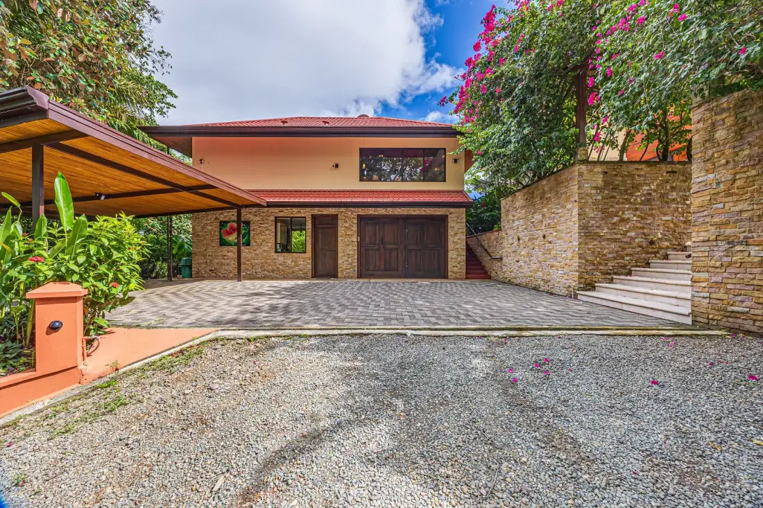 A house entrance with a paved driveway and garden greenery.