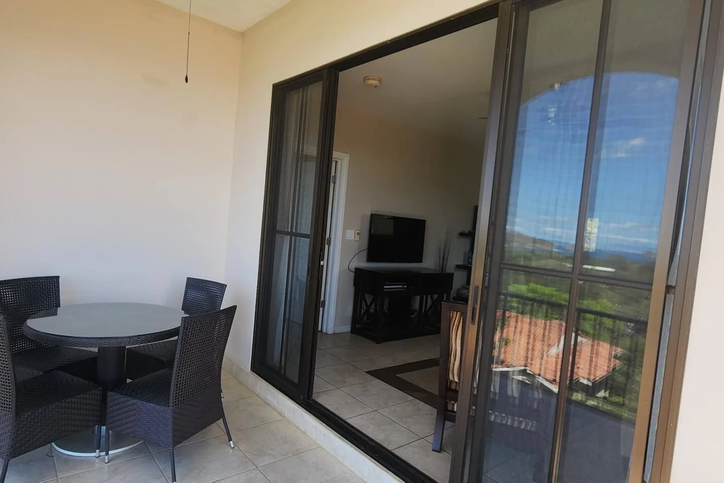 A tiled balcony with a round table and seating beside sliding glass doors.