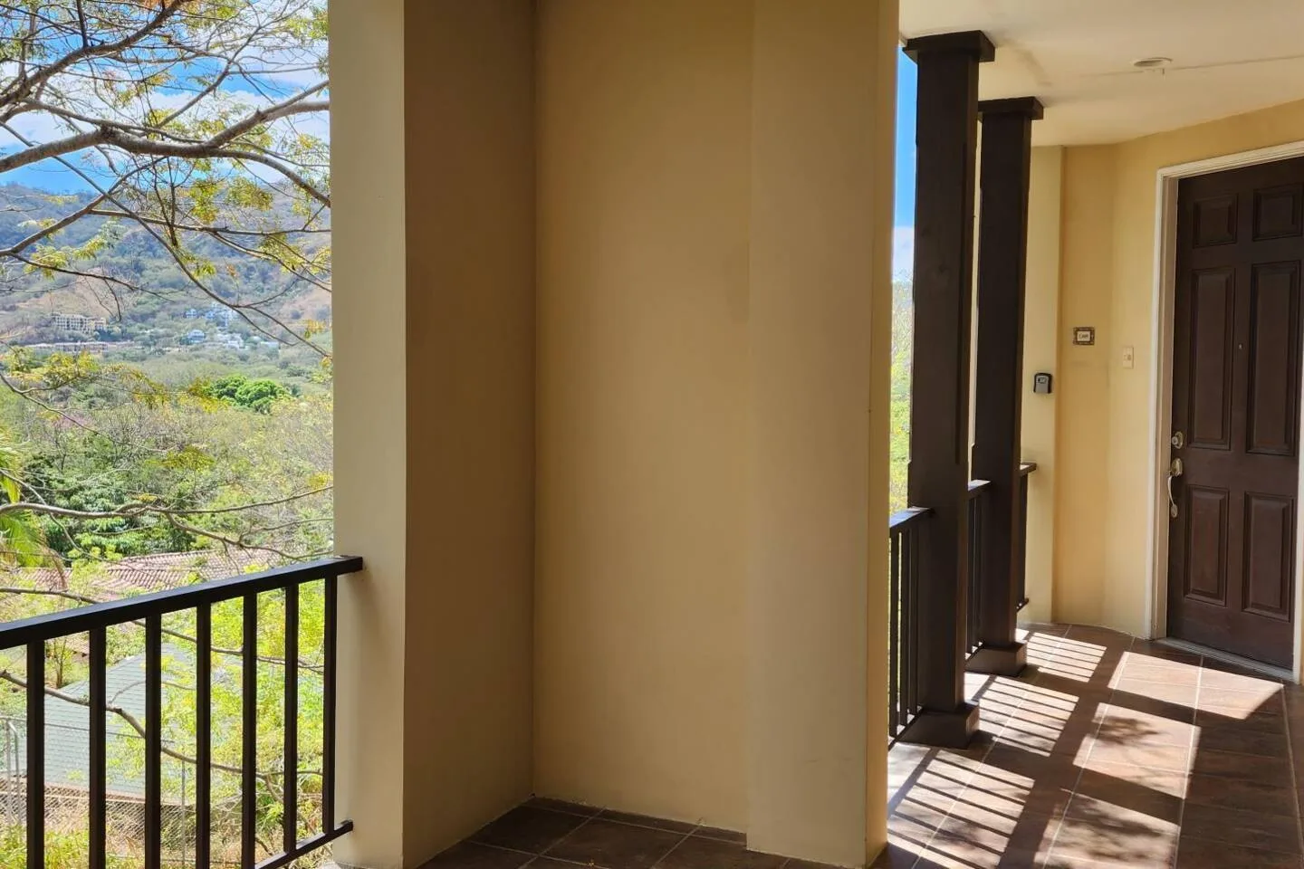 A sunlit balcony and covered entrance overlook a green mountain landscape.