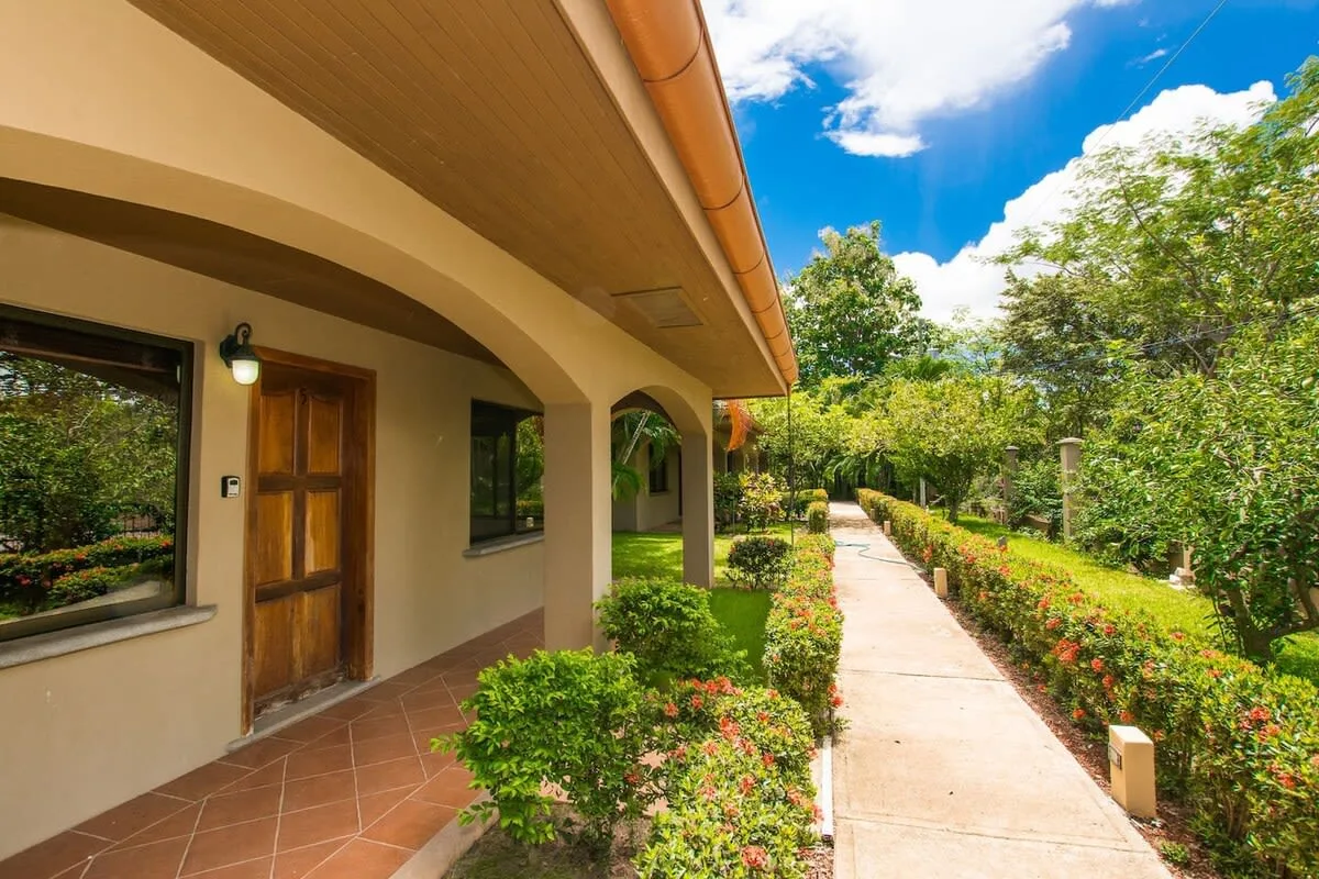 Un sendero de jardín bordea un edificio con una entrada cubierta de arcos.