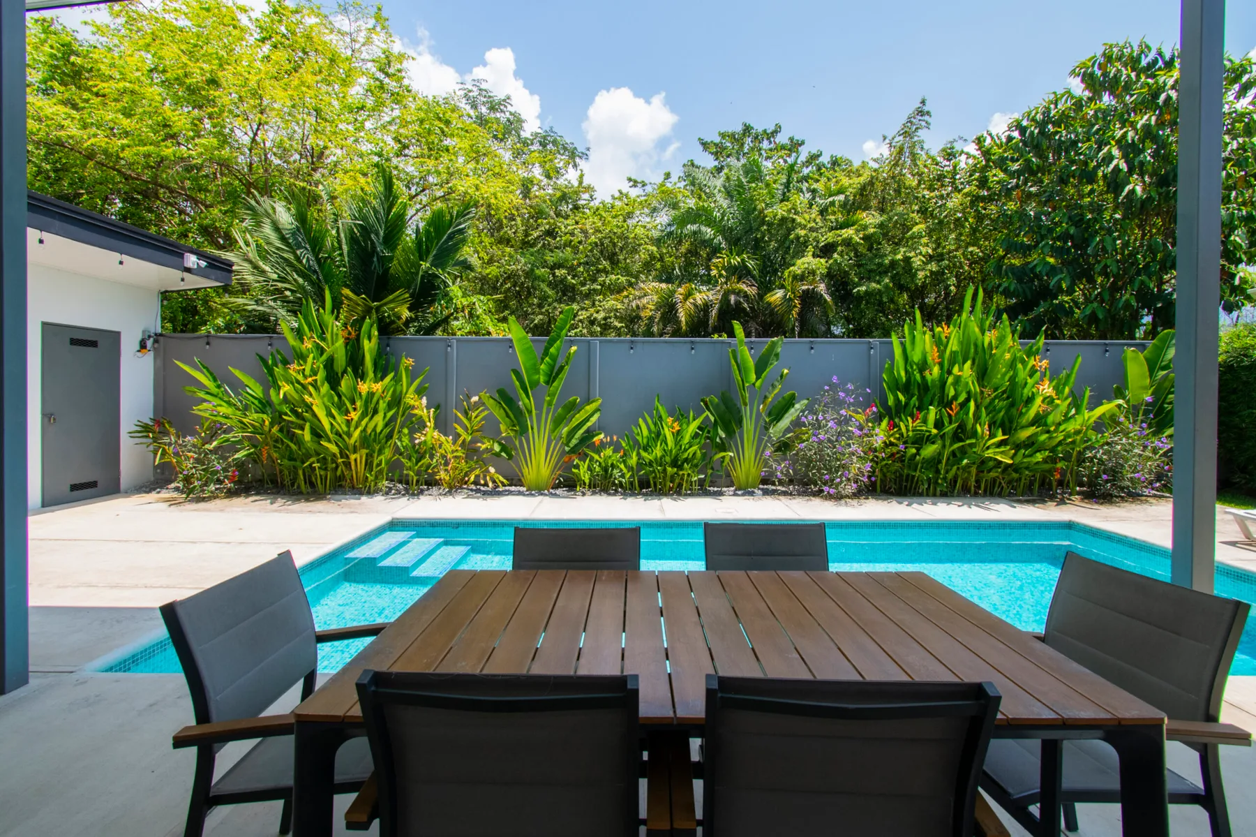Outdoor patio seating overlooks a swimming pool bordered by tropical greenery.