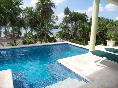Una piscina junto a palmeras tropicales, con el mar visible al fondo.