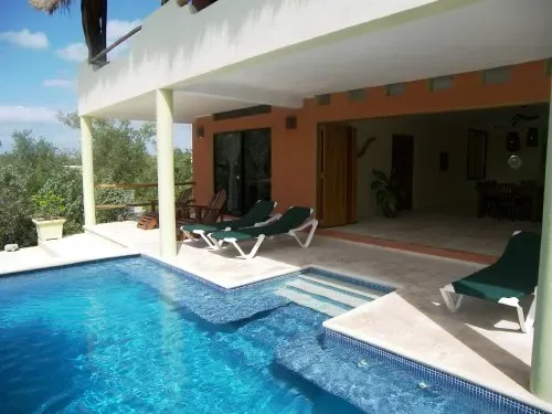 Una piscina junto a un patio cubierto con asientos reclinables.