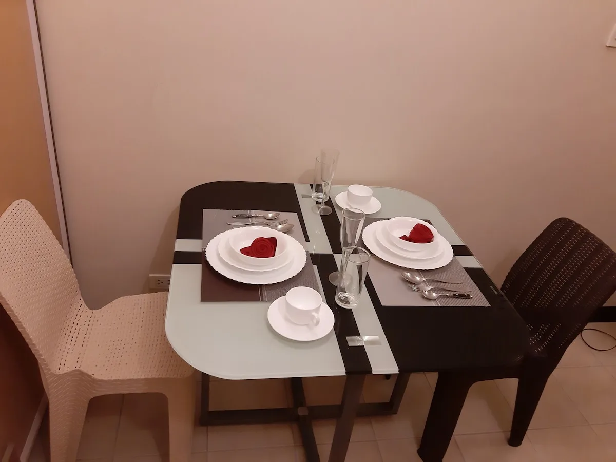 Una mesa de comedor está preparada con platos, tazas y cubiertos entre dos sillas.