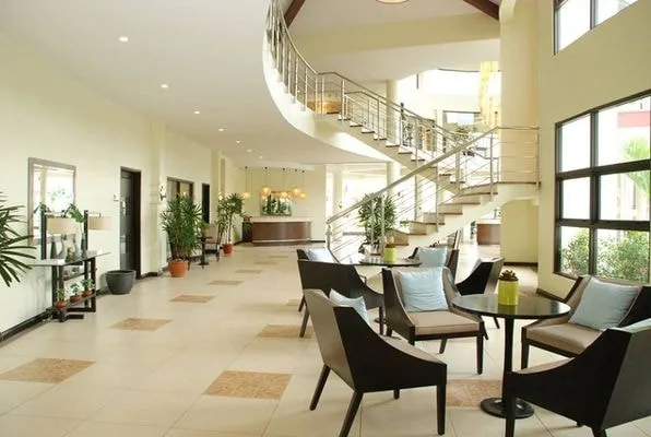 Un salón luminoso con asientos junto a grandes ventanas y una escalera curva.