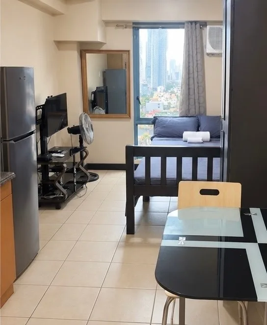 Una pequeña sala de estar con asientos, un televisor y una ventana amplia con vista a la ciudad.
