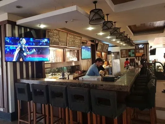 Una barra con asientos está frente a un televisor en un restaurante iluminado.
