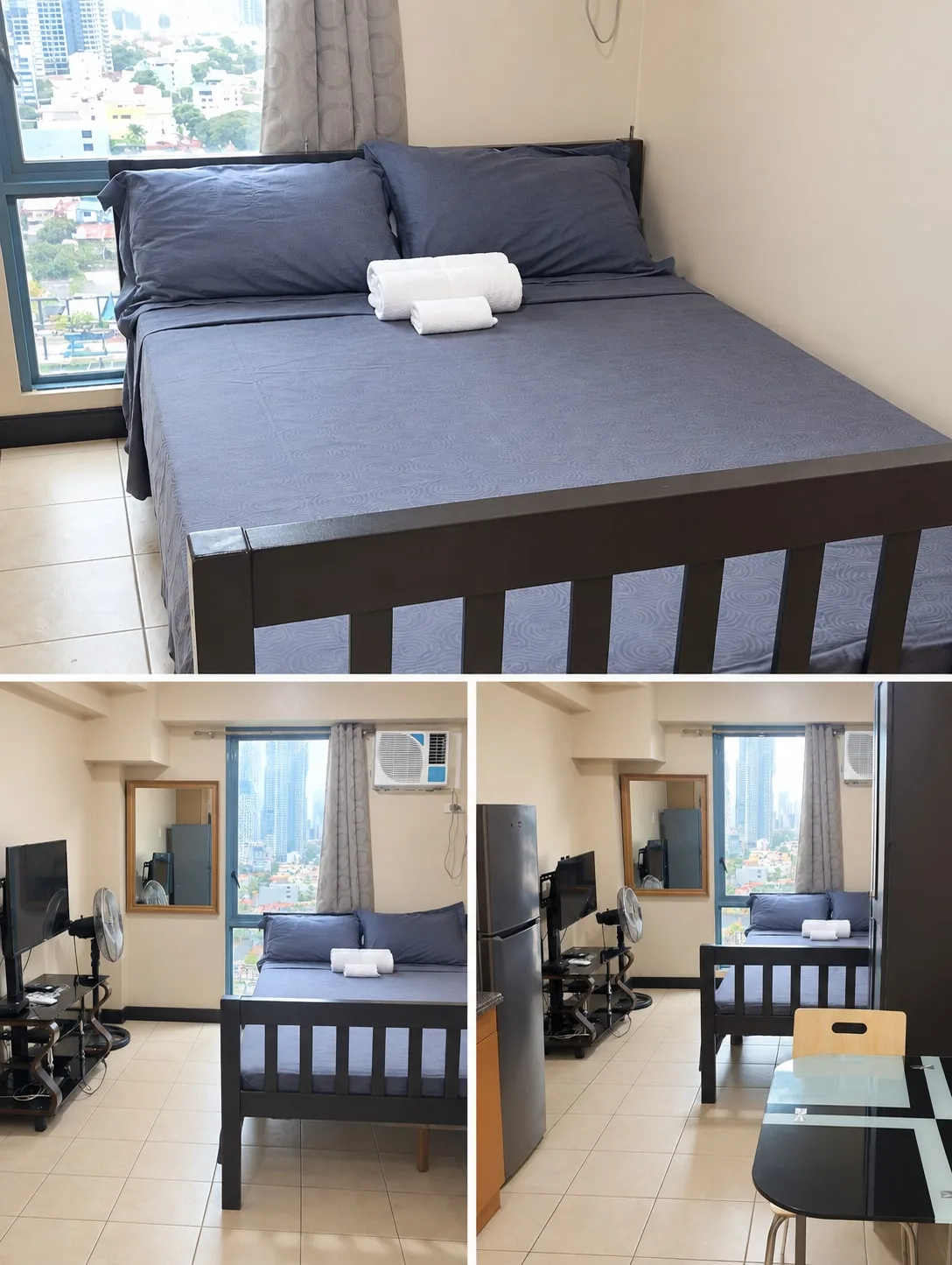 Un dormitorio con una cama gris junto a una ventana grande con vistas a edificios cercanos.