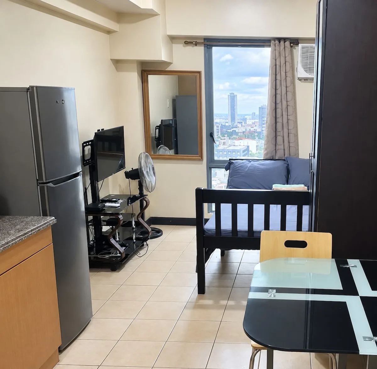 Una pequeña sala de estar con sofá, televisor y mesa de comedor junto a una ventana grande.