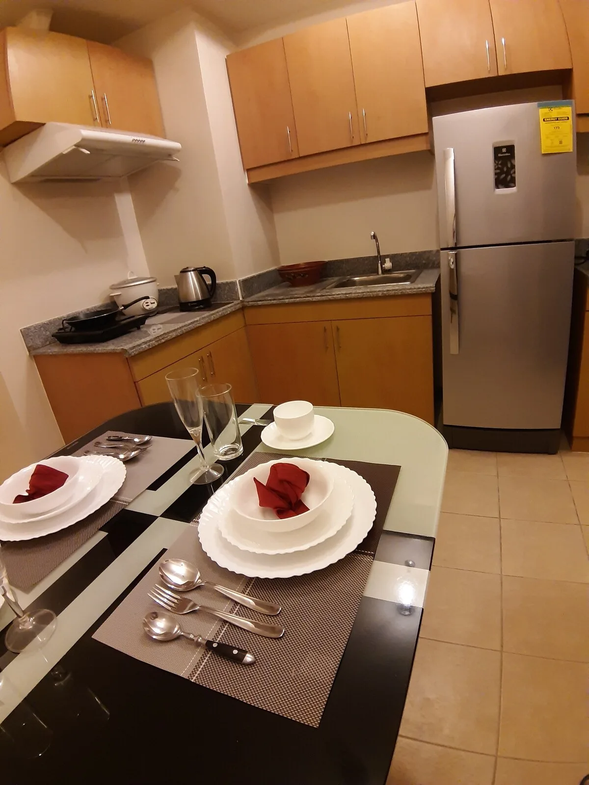Una cocina compacta con armarios de madera, un refrigerador y una mesa puesta con platos.