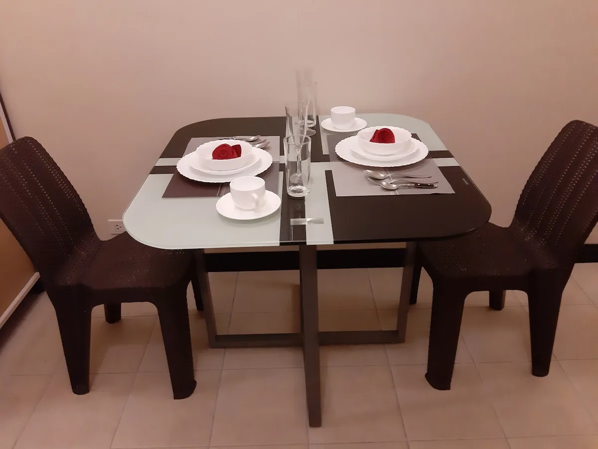 Zona de comedor con una mesa puesta y sillas oscuras de tejido trenzado.