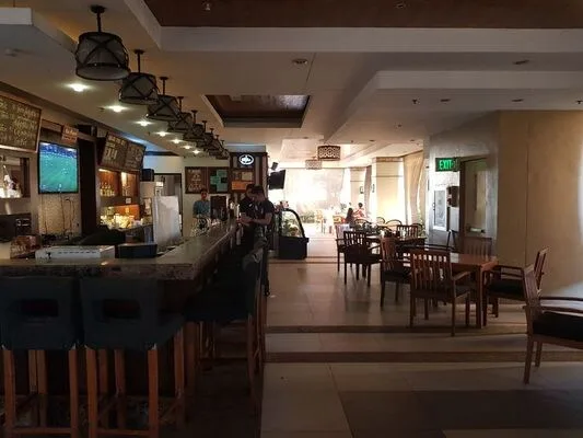 Comedor de un restaurante con mesas y sillas de madera junto a una barra larga.