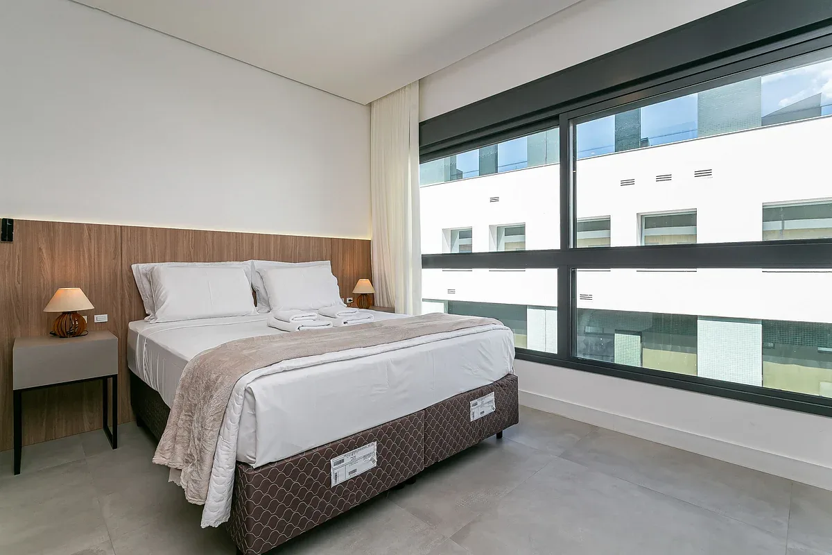 A bedroom with a neatly made bed beside a large window.