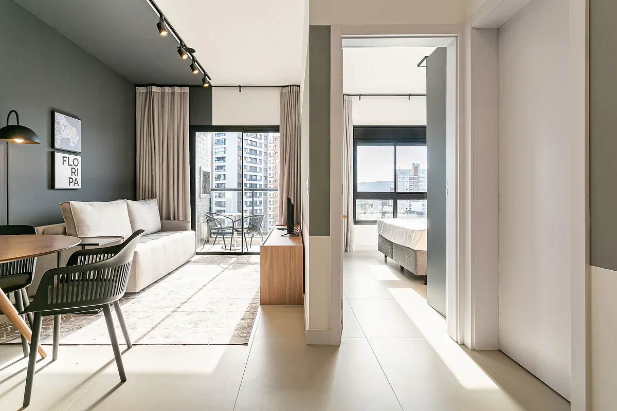 A bright open-plan living and dining area leads into a bedroom with large windows.