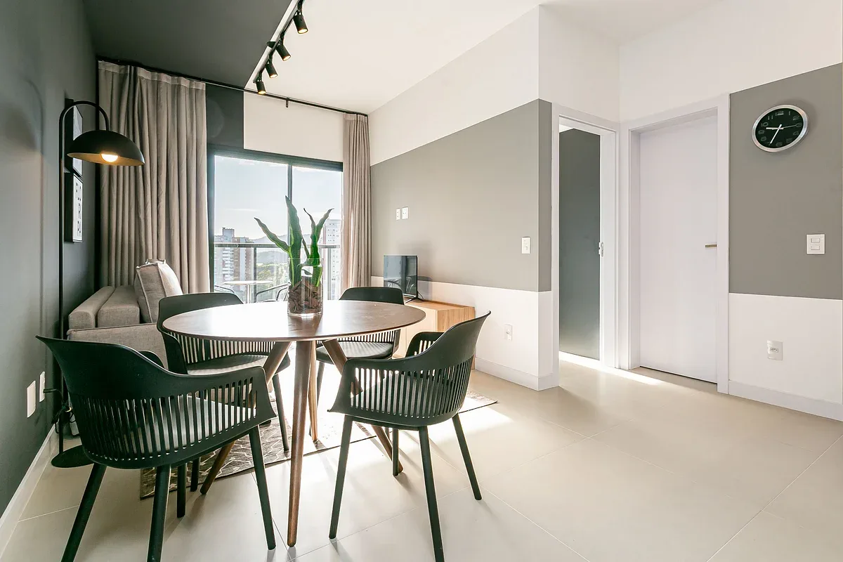 A dining area with a round table and chairs beside a large window.