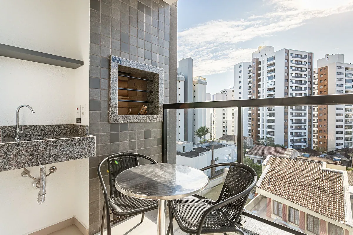 A balcony dining area with a round table and chairs overlooks nearby apartment buildings.