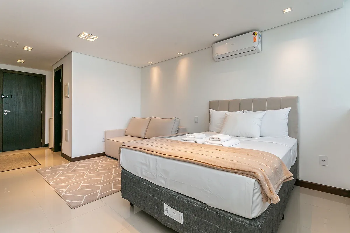 A bedroom with a bed and a small seating area beside the entrance.