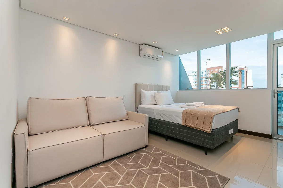 A bedroom with a bed, a sofa, and large windows.