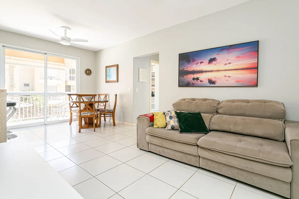 A bright living room with a beige sofa and dining table beside the balcony.