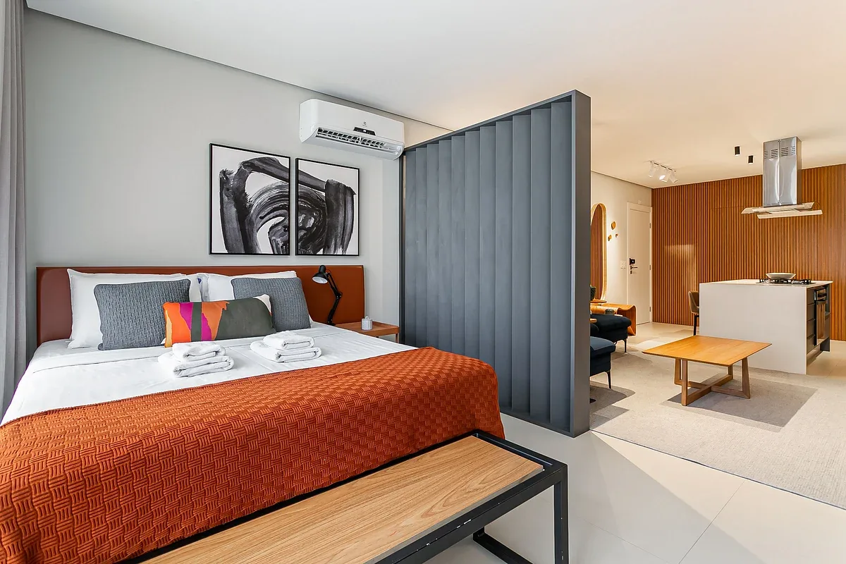 A bedroom with a bed beside a gray divider and an open living area.