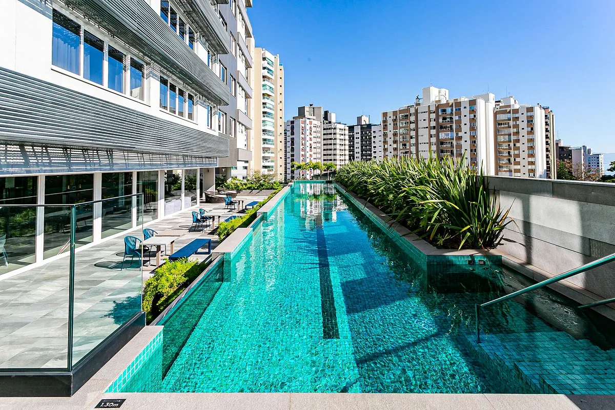 An outdoor swimming pool beside a modern building, with lounge seating along the edge.