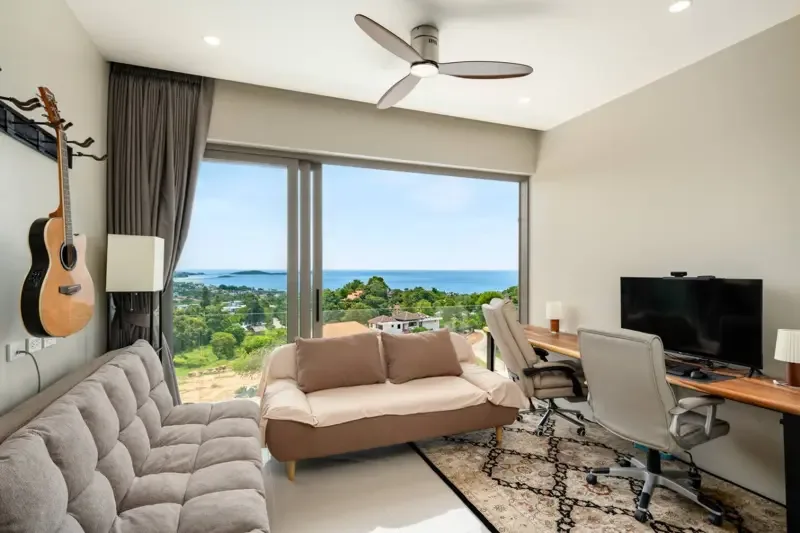 Una sala de estar luminosa con asientos y amplios ventanales con vistas al mar.