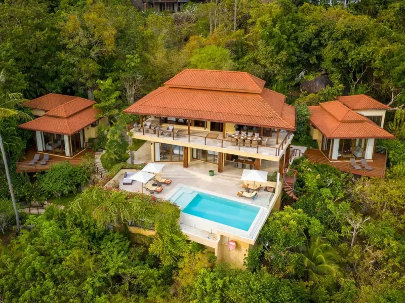 A large villa with a swimming pool sits amid dense green vegetation.