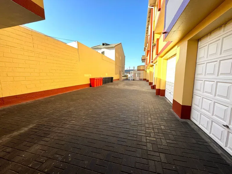 Un pasaje pavimentado transcurre entre un muro amarillo y fachadas coloridas.