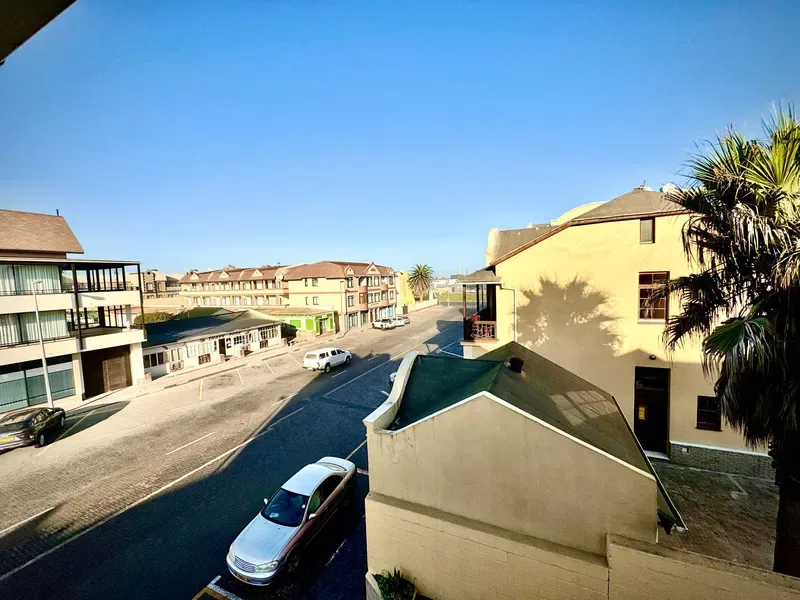 Una calle soleada con edificios bajos y coches estacionados.