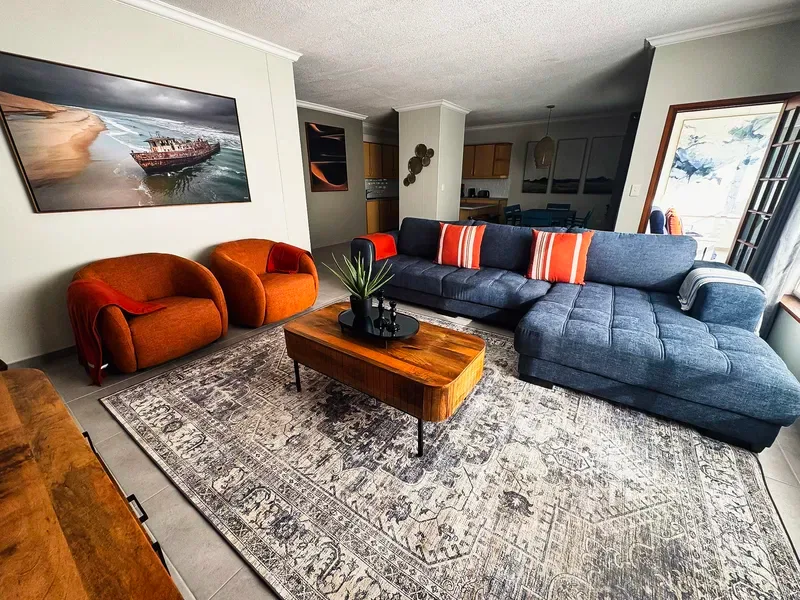 A living room with a large sectional sofa, orange seating, and a patterned rug.