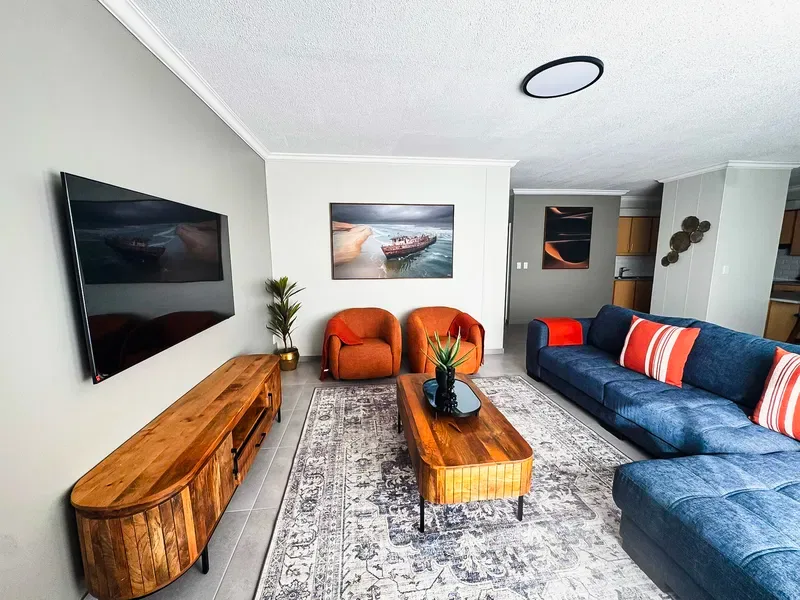 A living room with blue seating, wooden tables, and framed wall art.