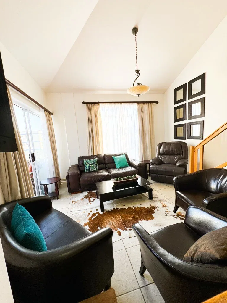 A living room with dark seating, a coffee table, and curtained windows.