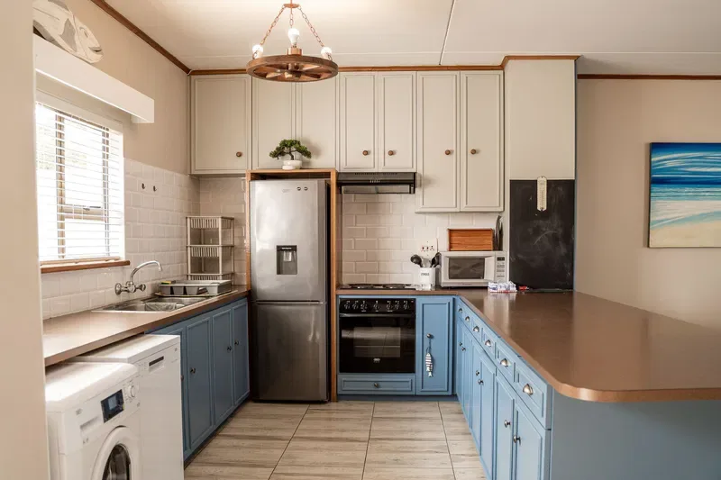 Una cocina luminosa con gabinetes azules, electrodomésticos de acero inoxidable y una encimera larga.