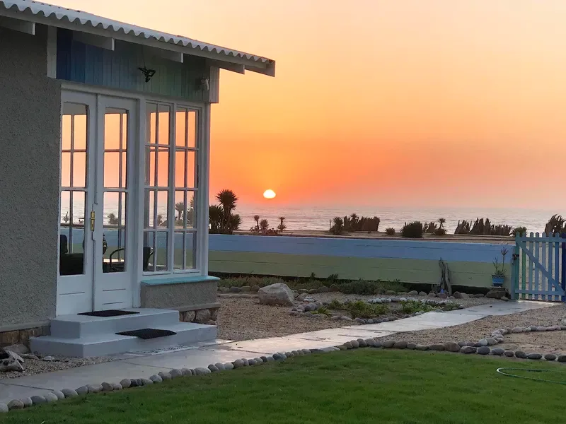 Una habitación junto al mar da a un césped y al océano al atardecer.