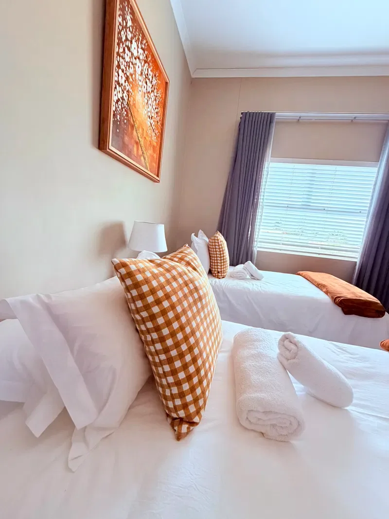 A bedroom with two neatly made beds and a window with blinds.