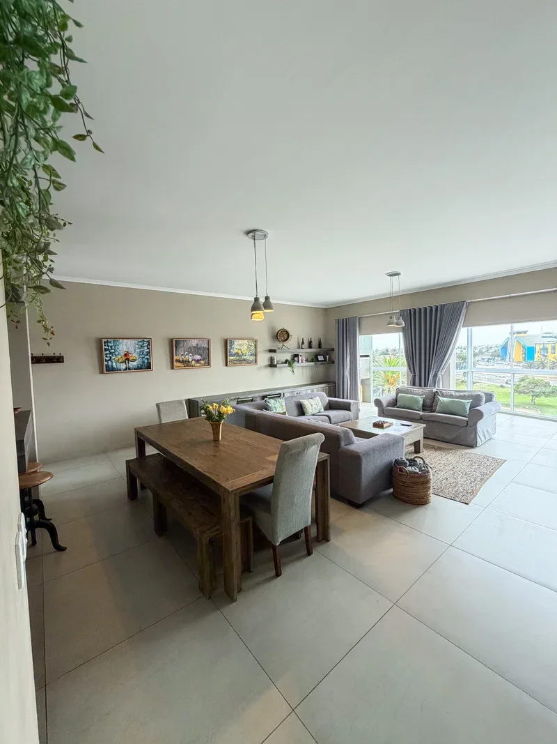 A bright open-plan living and dining area with seating beside large windows.