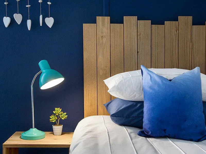 A bedroom with a bed, blue pillows, and a wooden headboard.