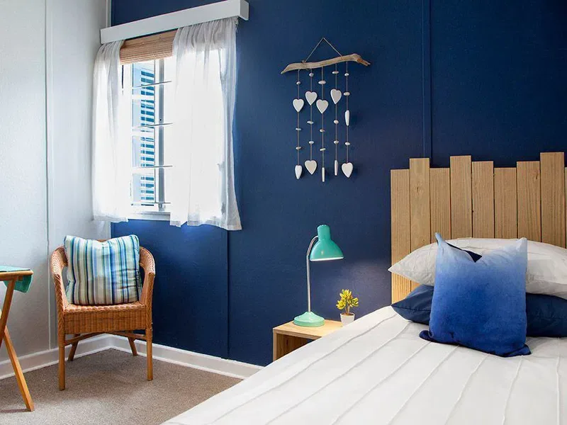 A bedroom with a bed, a wicker chair, and a blue accent wall.