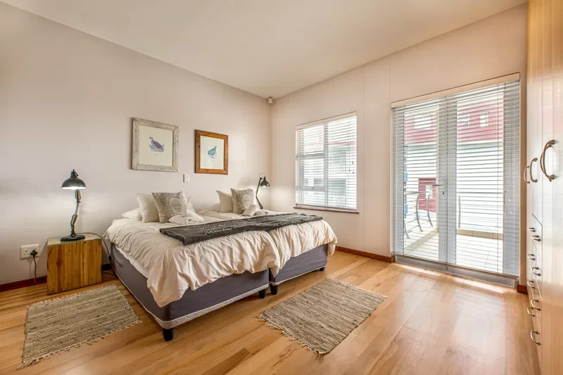 A bright bedroom with a bed, bedside tables, and large windows.