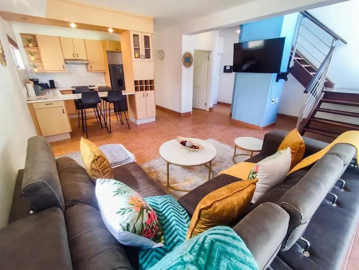 Una sala de estar con una zona de asientos, mesas de centro y una cocina abierta.