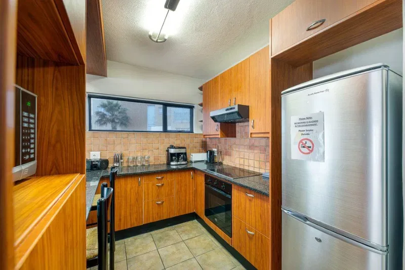 Una cocina compacta con gabinetes de madera, paredes de azulejos y electrodomésticos de acero inoxidable.