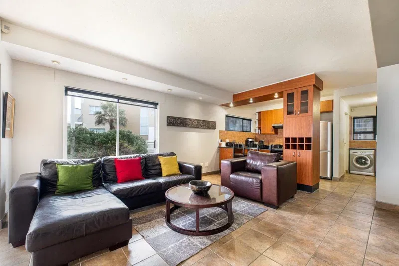 Una sala de estar con asientos oscuros y una mesa de centro redonda junto a la cocina.