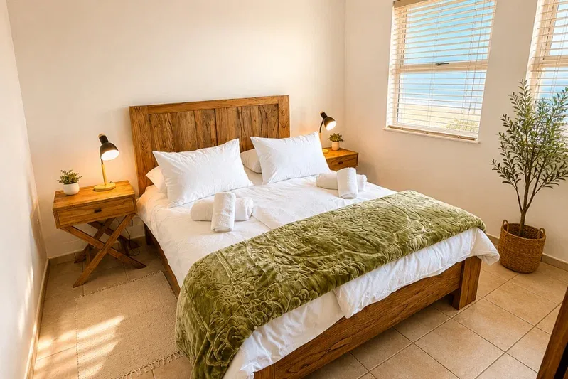 A bedroom with a wooden bed, white bedding, and a green throw.