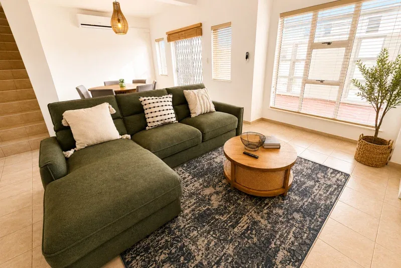 A bright living room with green seating, a round coffee table, and large windows.