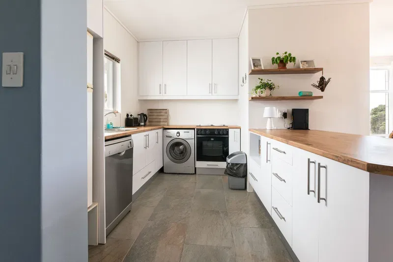 Una cocina luminosa con gabinetes blancos, una encimera larga y electrodomésticos de acero inoxidable.