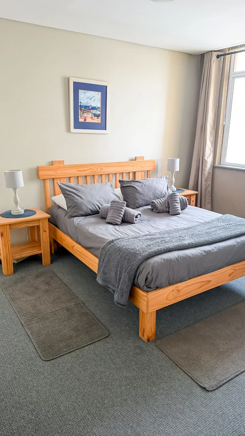 Un dormitorio con una cama de madera, ropa de cama gris y mesitas a juego.