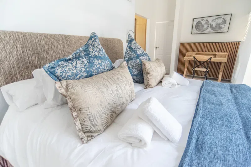 Un dormitorio con una cama bien tendida, cojines estampados y una manta azul.