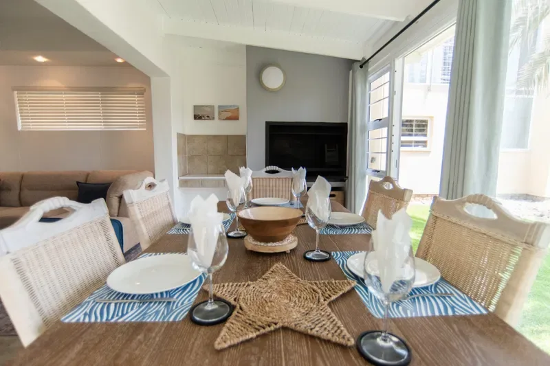 Comedor con la mesa puesta, sillas tejidas y una chimenea.